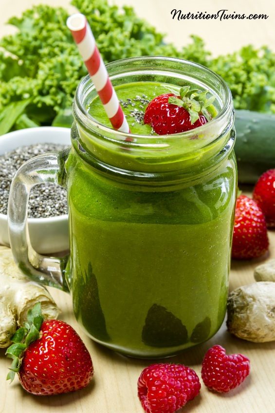 30923722 - healthy green juice smoothie surrounded by whole fruits, vegetables and chia seeds with fresh strawberry garnish and red swirl straw