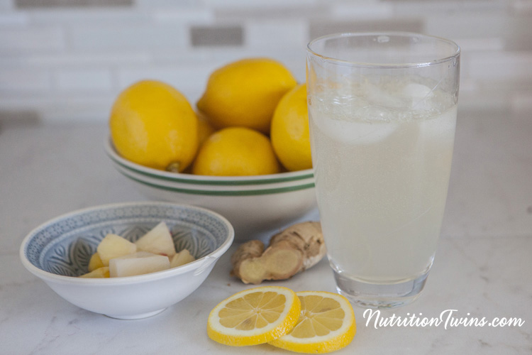 Glass of Pineapple Ginger Lemon DIY Soda with bowl of lemons, bowl of pineapple cubes, lemon slices and ginger root